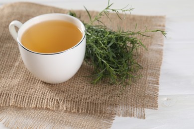 Photo of Aromatic herbal tea and fresh tarragon sprigs on white wooden table