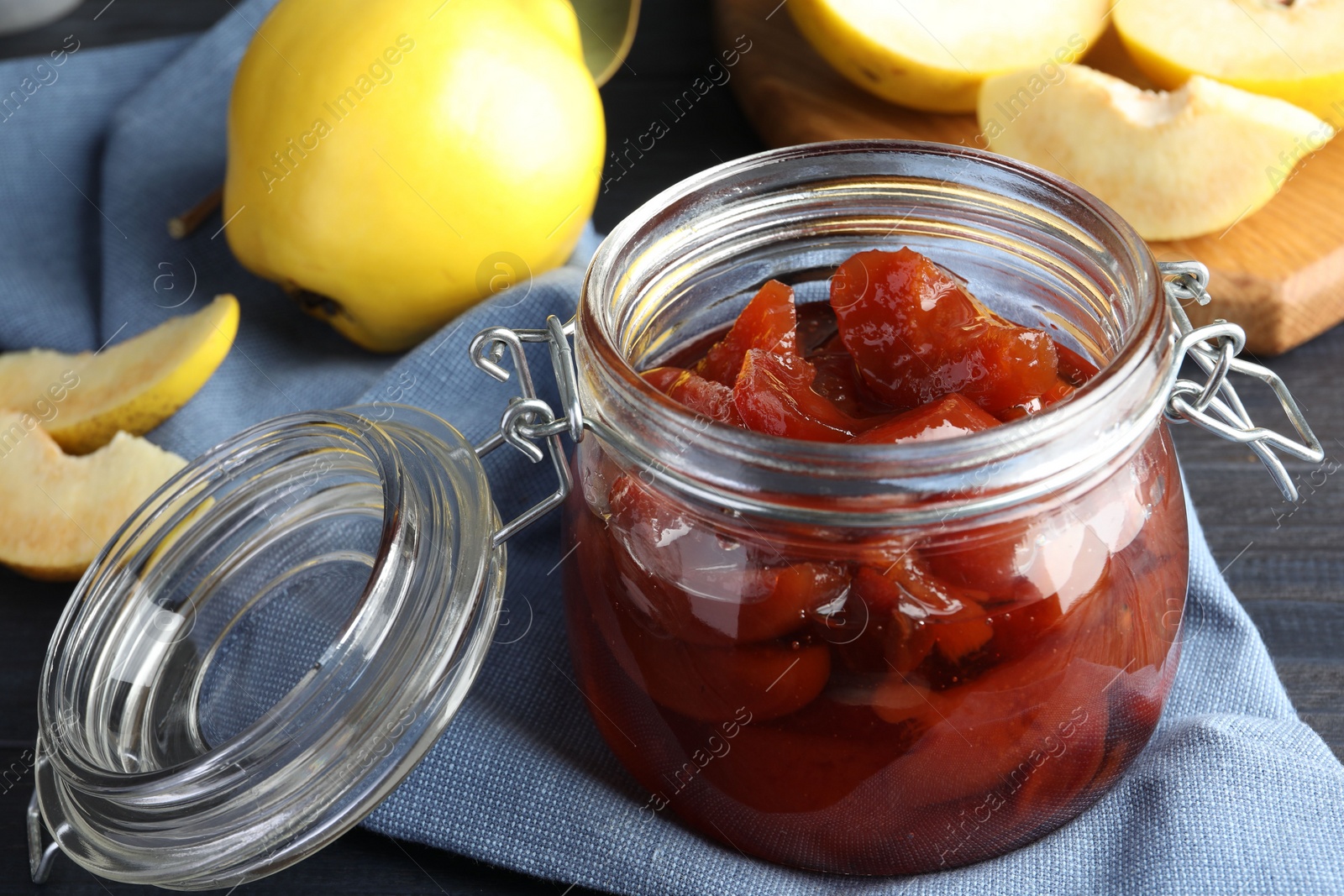 Photo of Quince jam in glass jar and fresh raw fruits on grey table, closeup