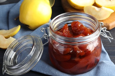 Photo of Quince jam in glass jar and fresh raw fruits on grey table, closeup