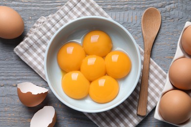 Photo of Chicken eggs and bowl with raw yolks on grey wooden table, flat lay