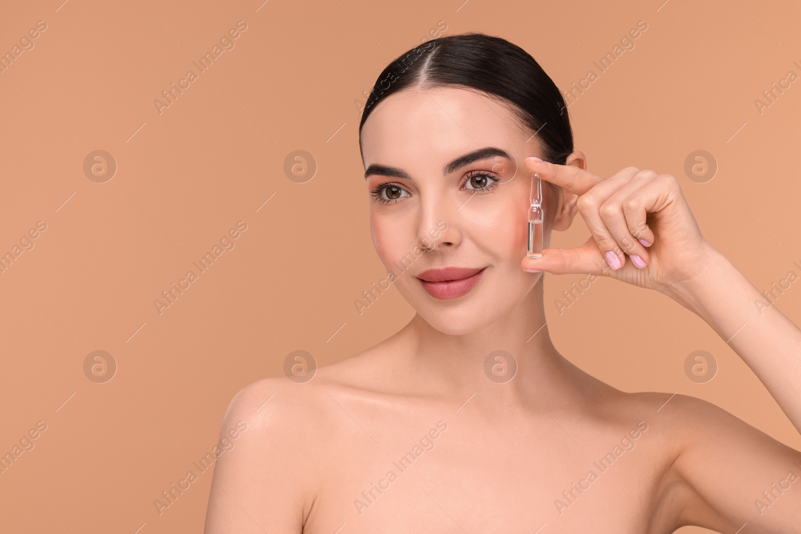 Photo of Beautiful young woman holding skincare ampoule on beige background. Space for text