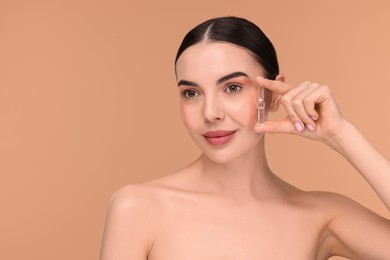 Beautiful young woman holding skincare ampoule on beige background. Space for text