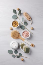 Flat lay composition with different spa products, burning candle and eucalyptus branches on light wooden table