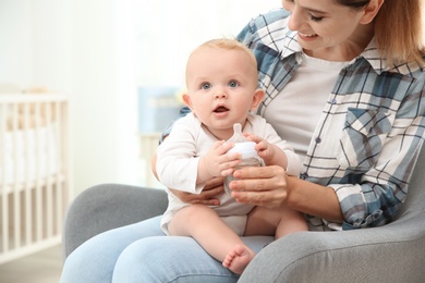 Lovely mother giving her baby drink from bottle in room