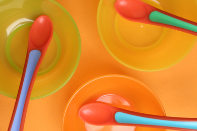 Set of colorful plastic dishware on orange background, flat lay. Serving baby food
