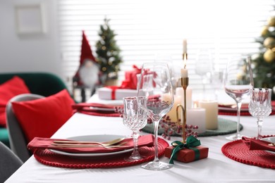 Christmas table setting with burning candles, gift box and dishware indoors