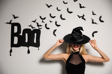 Woman in witch hat posing near white wall decorated for Halloween