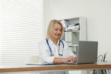 Photo of Doctor working on laptop at wooden table in clinic