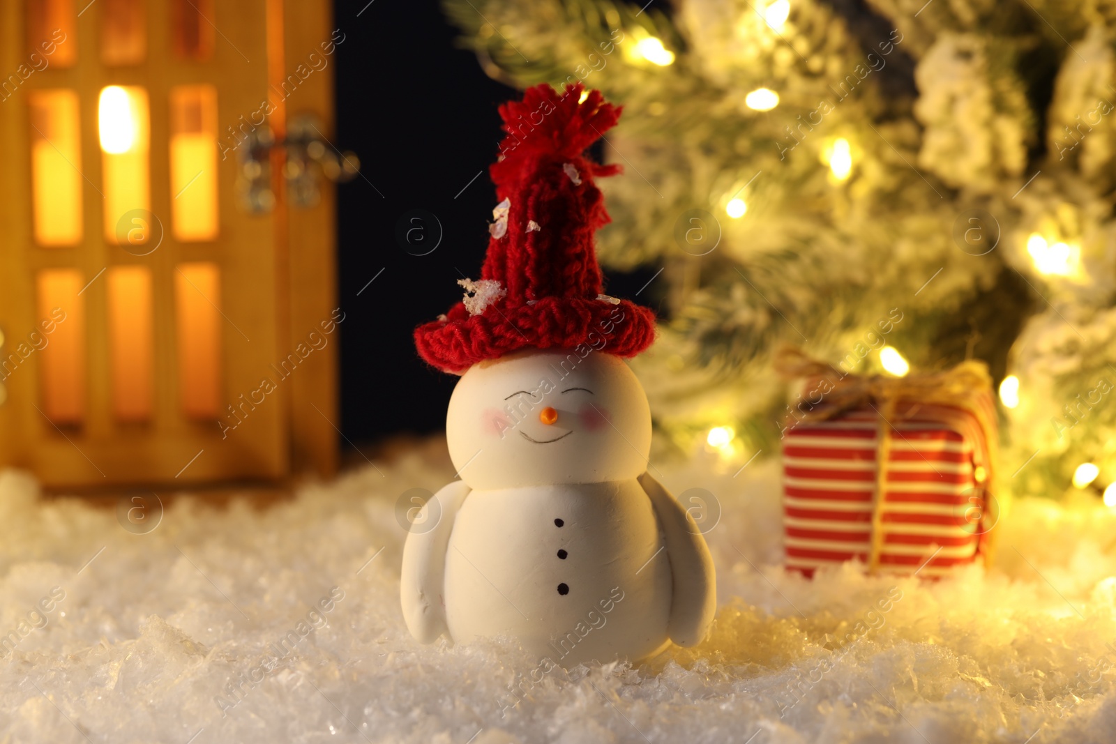 Photo of Cute decorative snowman, lantern, gift box and Christmas tree on artificial snow, closeup