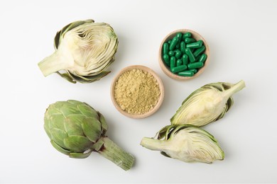 Bowls with pills, powder and fresh artichokes on white background, flat lay