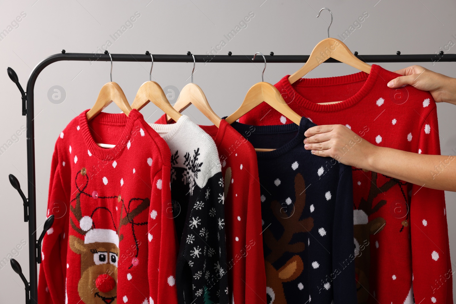 Photo of Woman picking Christmas sweater from rack near light wall, closeup