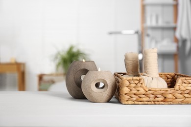 Photo of Burning candles, spa herbal bags and stones on white table in bathroom, space for text