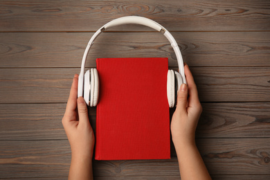 Woman with book and headphones on wooden table, top view