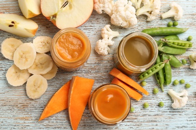 Jars with healthy baby food and ingredients on wooden table, top view