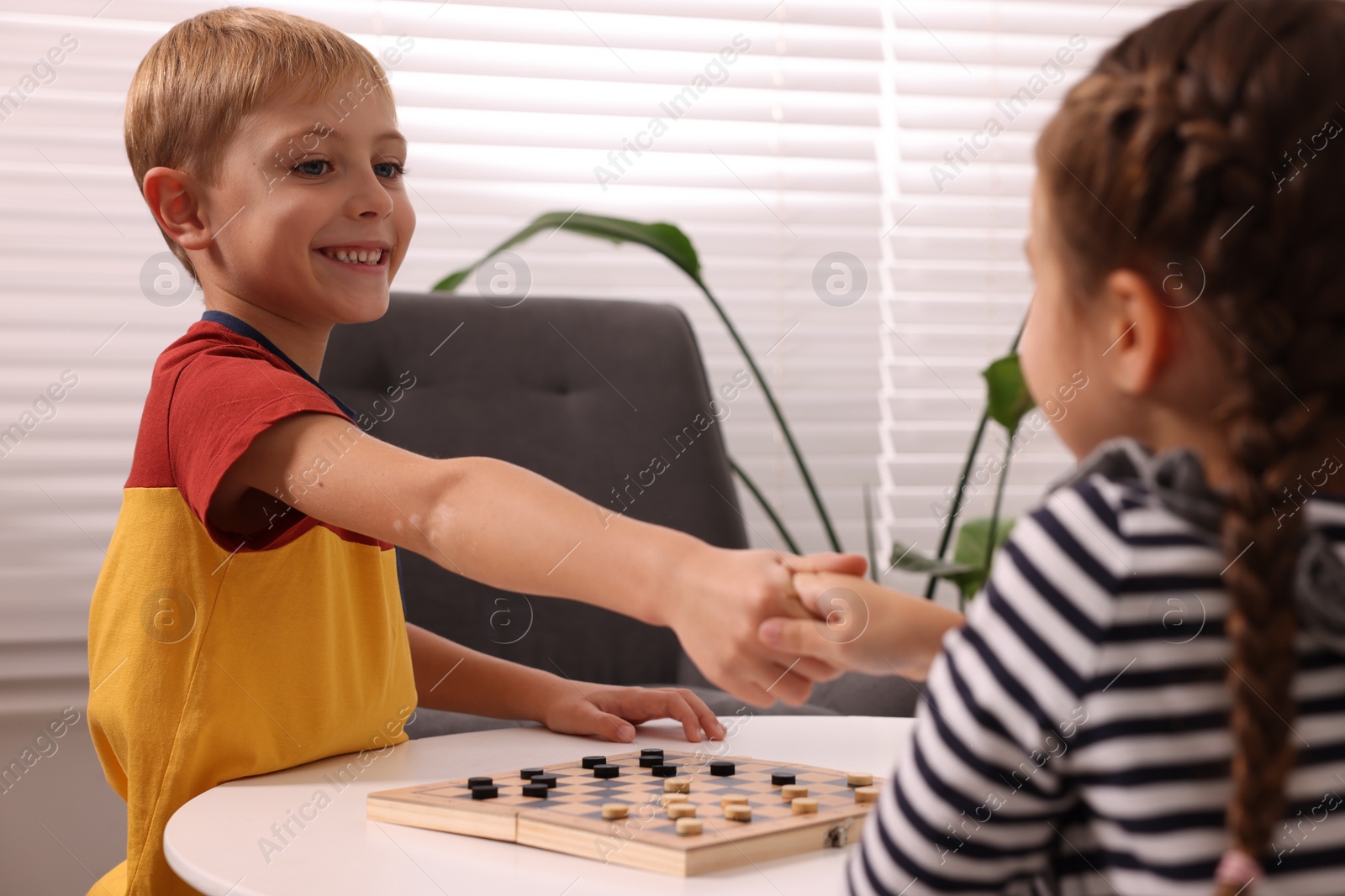 Photo of Children shaking hands after playing checkers at coffee table indoors