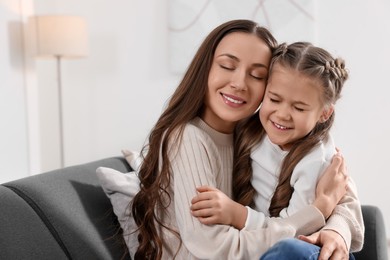 Photo of Happy mother hugging her cute daughter on sofa at home