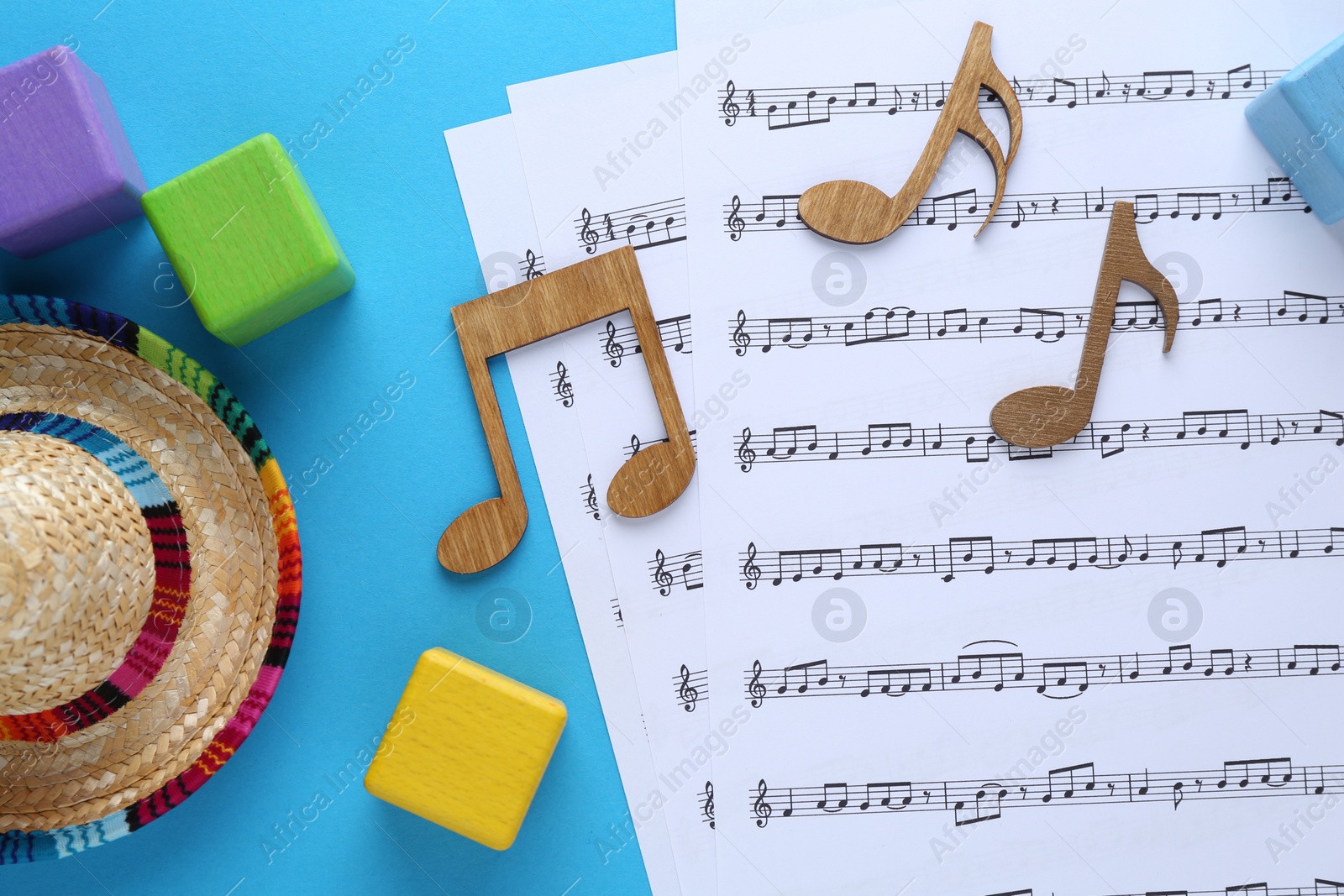 Photo of Baby songs. Music sheets, wooden notes, cubes and hat on light blue background, flat lay