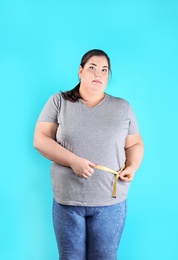 Overweight woman measuring waist before weight loss on color background