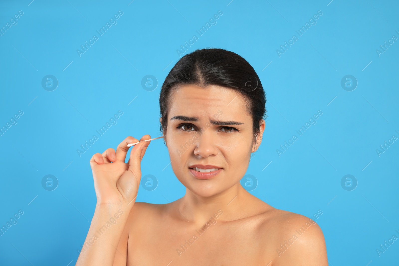 Photo of Young woman cleaning ear with cotton swab on light blue background