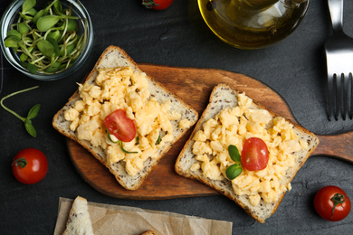 Photo of Tasty scrambled egg sandwiches served on black table, flat lay