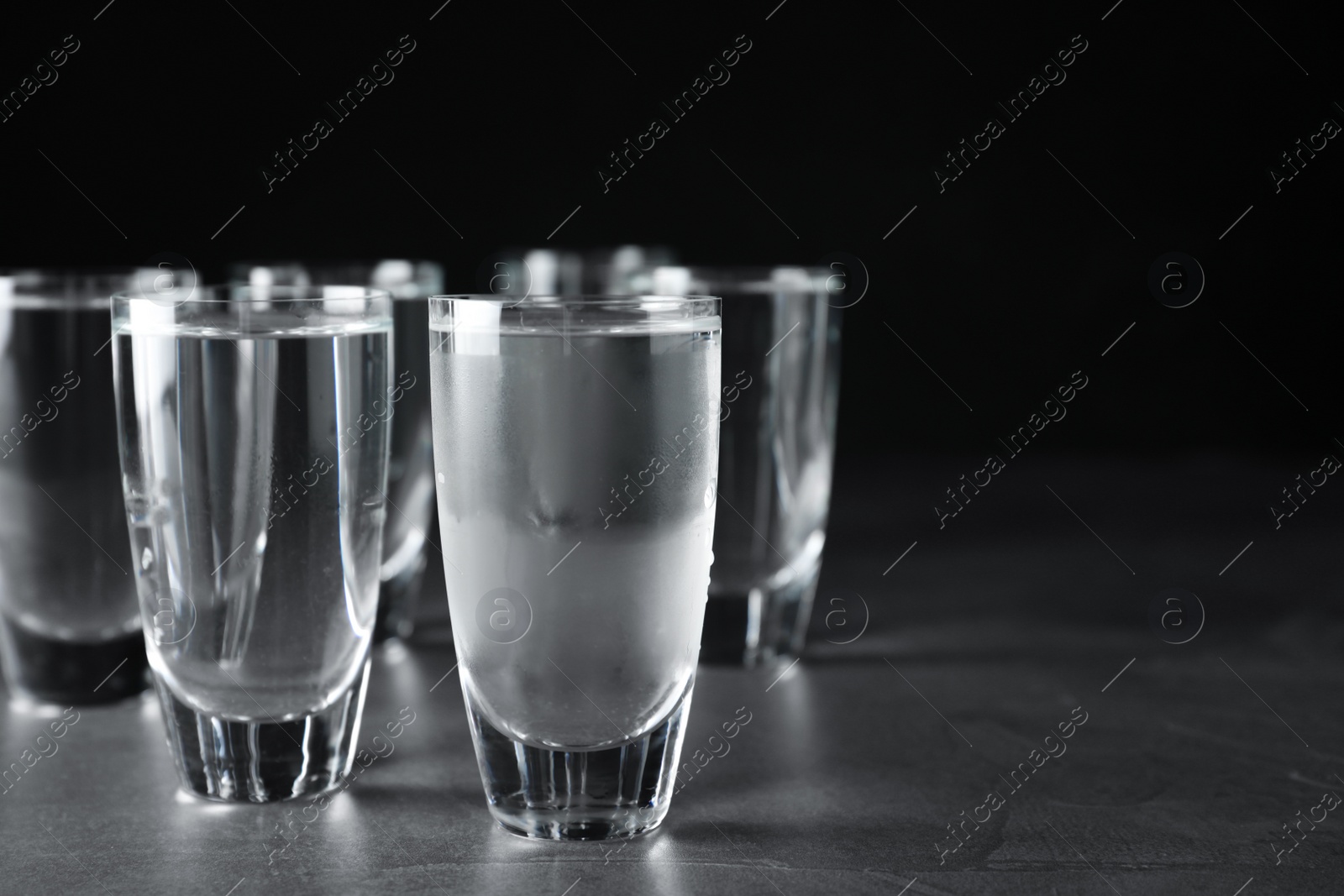 Photo of Shots of vodka on grey table against black background. Space for text