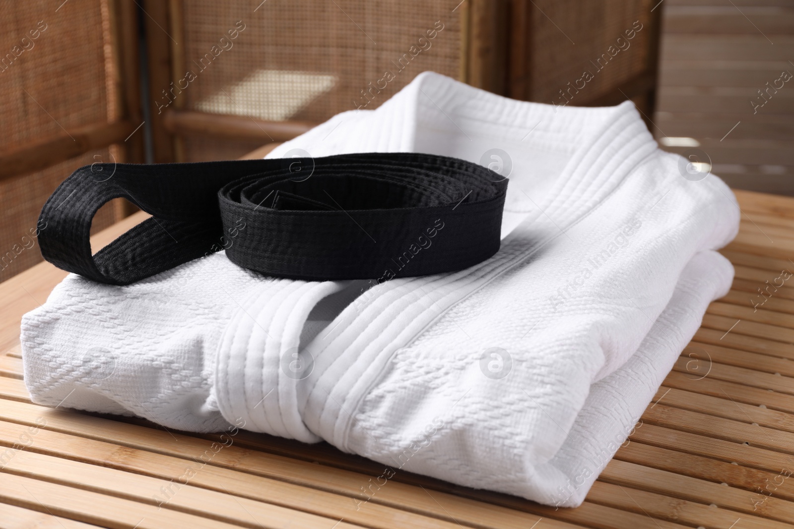 Photo of Martial arts uniform with black belt on table indoors