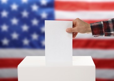 Election in USA. Man putting his vote into ballot box against national flag of United States, closeup