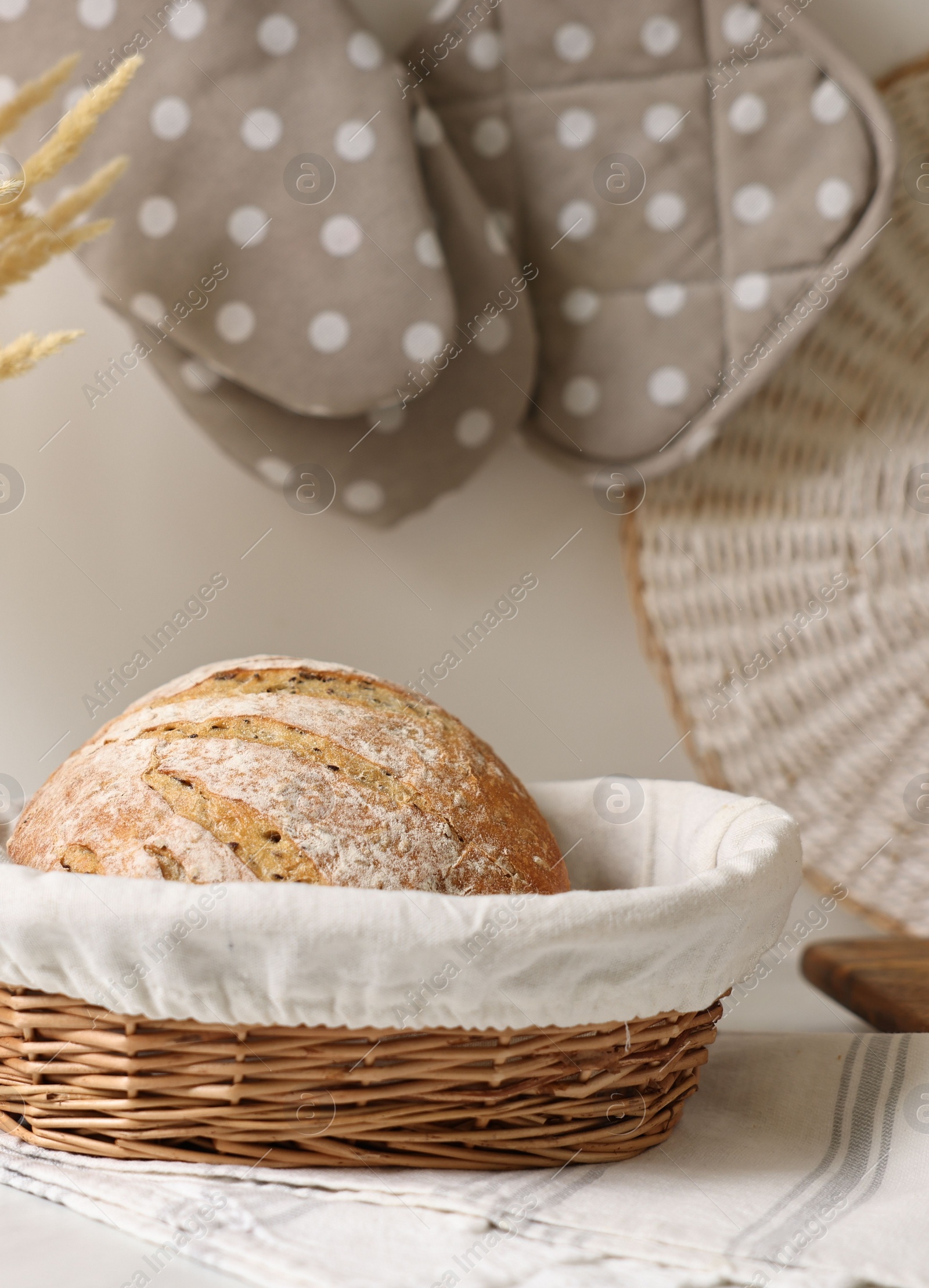 Photo of Wicker bread basket with freshly baked loaf on white marble table in kitchen