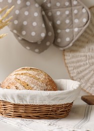 Wicker bread basket with freshly baked loaf on white marble table in kitchen