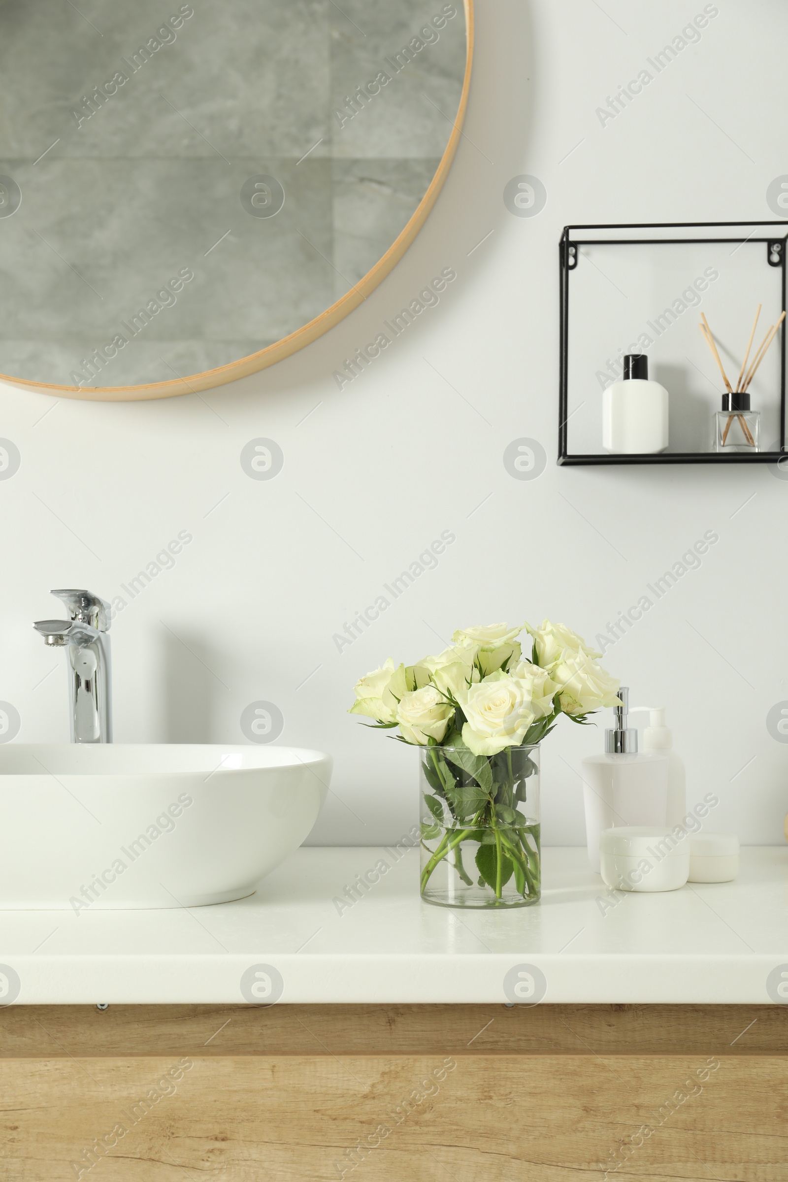 Photo of Bouquet of beautiful roses in vase and bath accessories near sink in bathroom