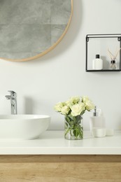 Bouquet of beautiful roses in vase and bath accessories near sink in bathroom