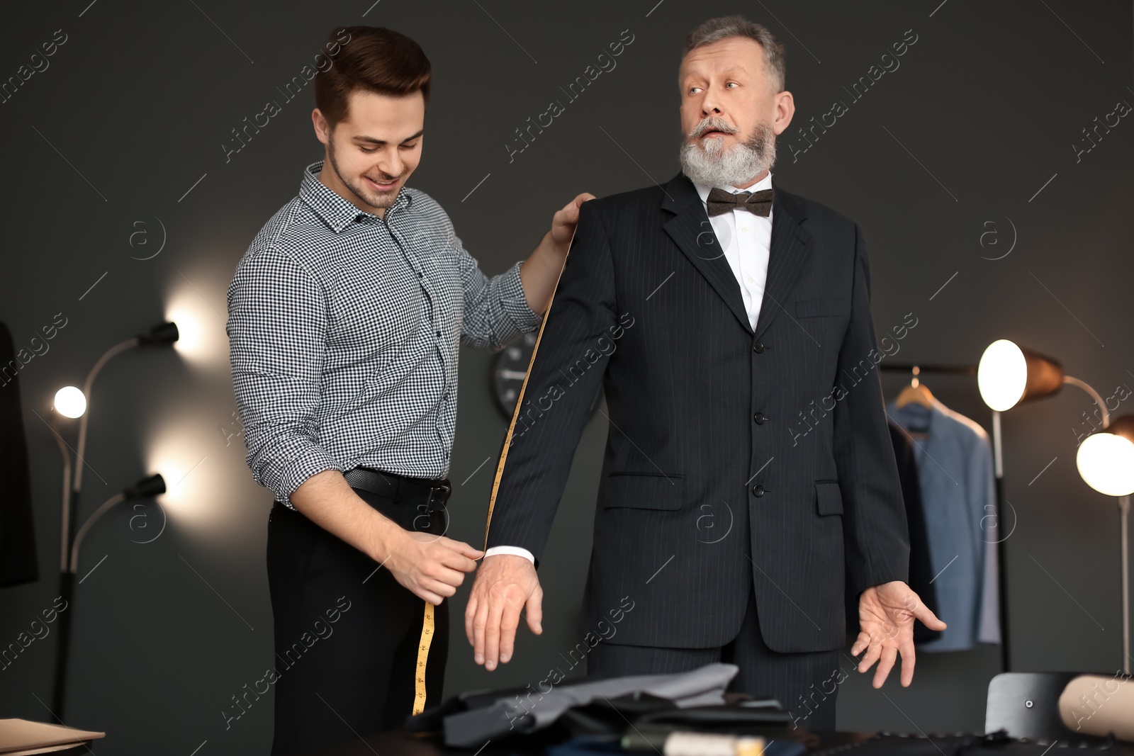 Photo of Young tailor taking client's measurements in atelier