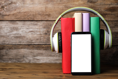 Books with modern headphones and smartphone on wooden table. Space for text