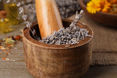 Mortar with pestle and dry lavender flowers on wooden table, closeup. Medicinal herbs