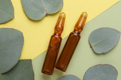 Pharmaceutical ampoules with medication and eucalyptus leaves on color background, flat lay