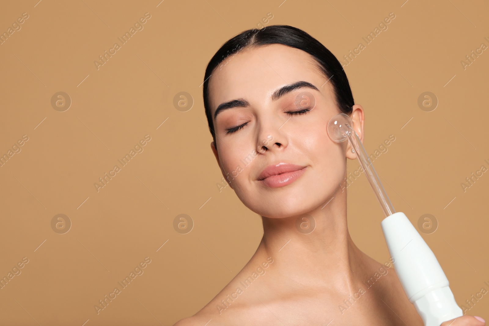 Photo of Woman using high frequency darsonval device on beige background. Space for text