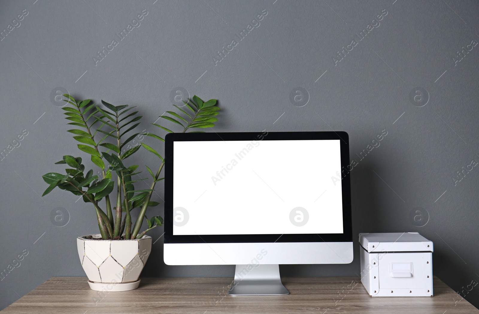 Photo of Modern computer monitor on table against gray wall. Mock up with space for text