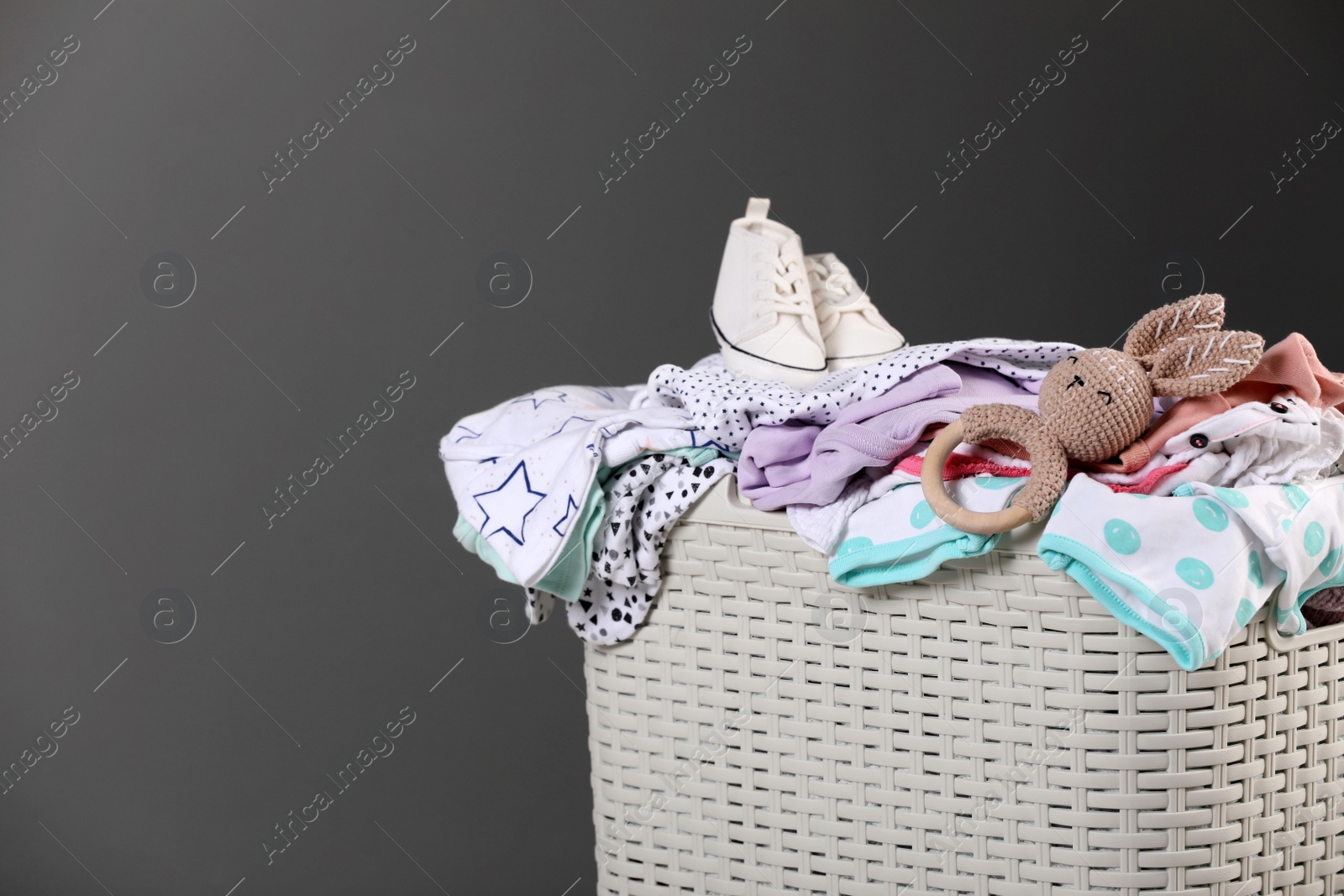 Photo of Laundry basket with baby clothes, shoes and crochet toy on grey background, closeup. Space for text
