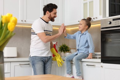Photo of Spring cleaning. Father and daughter giving high five in kitchen
