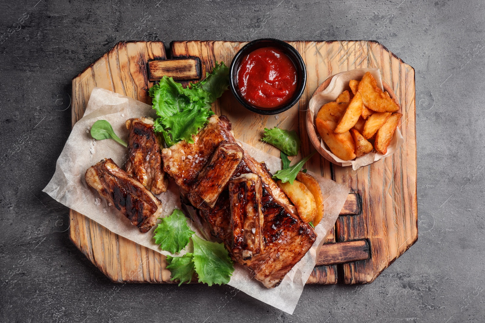 Photo of Delicious grilled ribs and garnish on grey table, top view