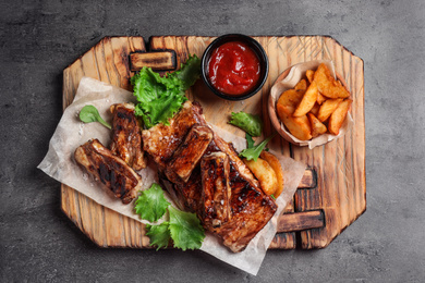 Photo of Delicious grilled ribs and garnish on grey table, top view