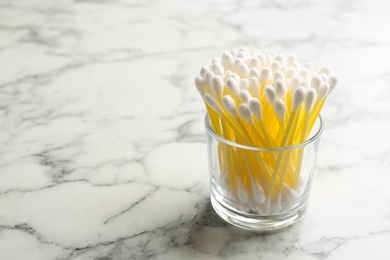 Photo of Glass with cotton swabs on marble background. Space for text