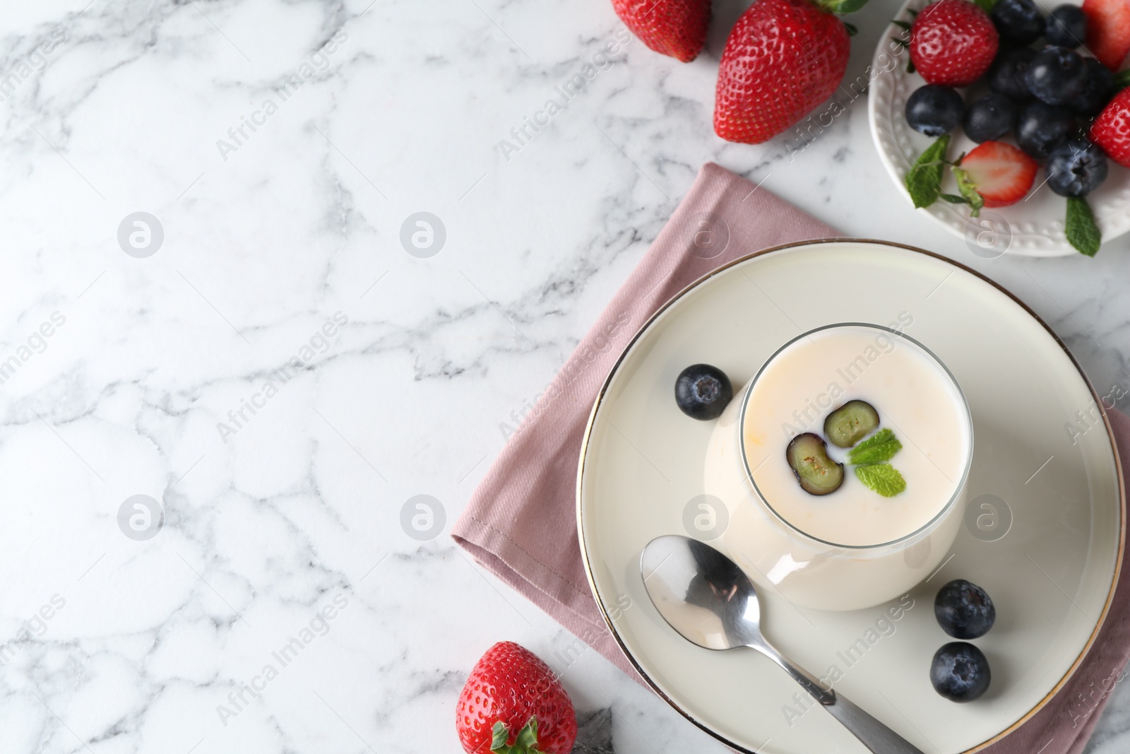 Photo of Tasty yogurt in glass and berries on white marble table, flat lay. Space for text