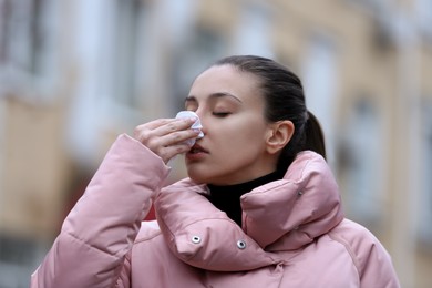 Ill woman with paper tissue sneezing outdoors