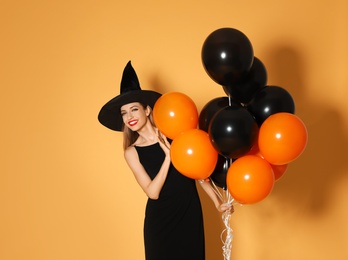Photo of Beautiful woman wearing witch costume with balloons for Halloween party on yellow background, space for text
