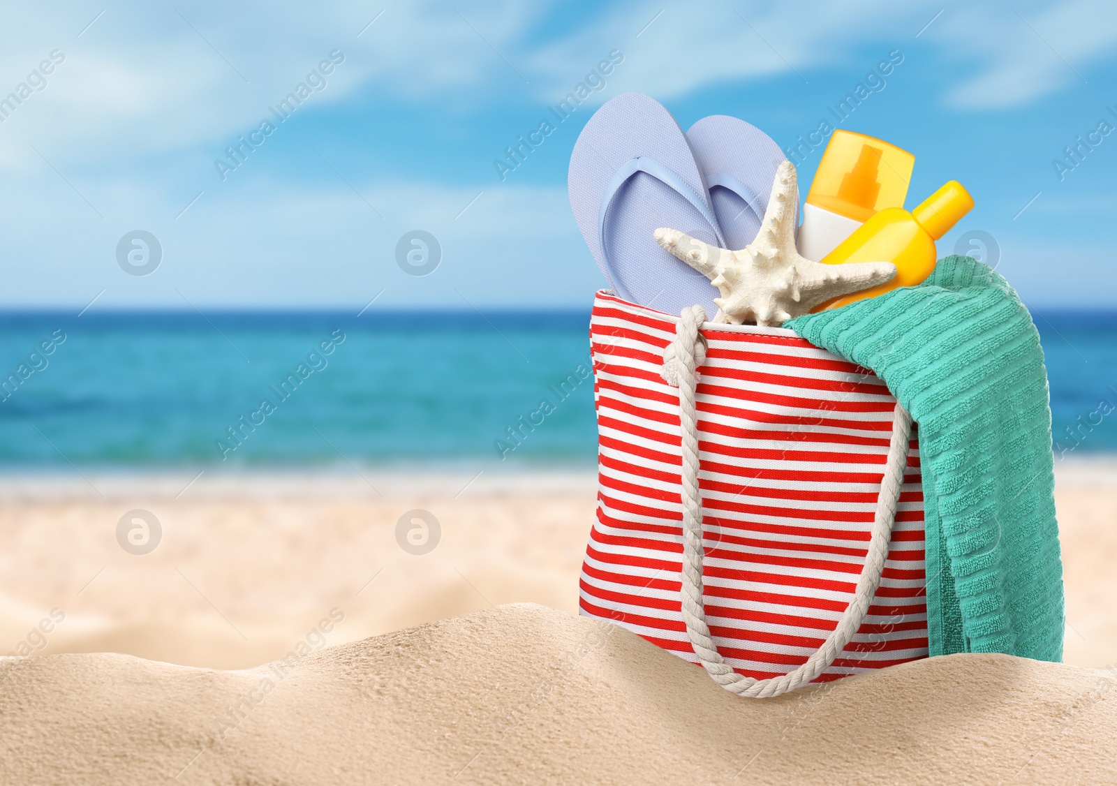 Image of Stylish bag with different accessories on sandy beach near ocean, space for text 