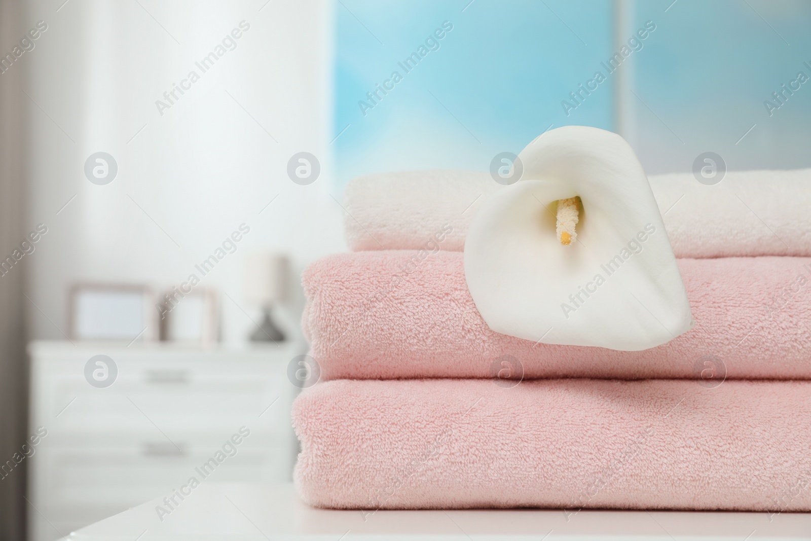 Photo of Stack of clean towels with flower on table in room. Space for text