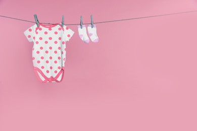 Baby onesie and socks drying on laundry line against pink background, space for text