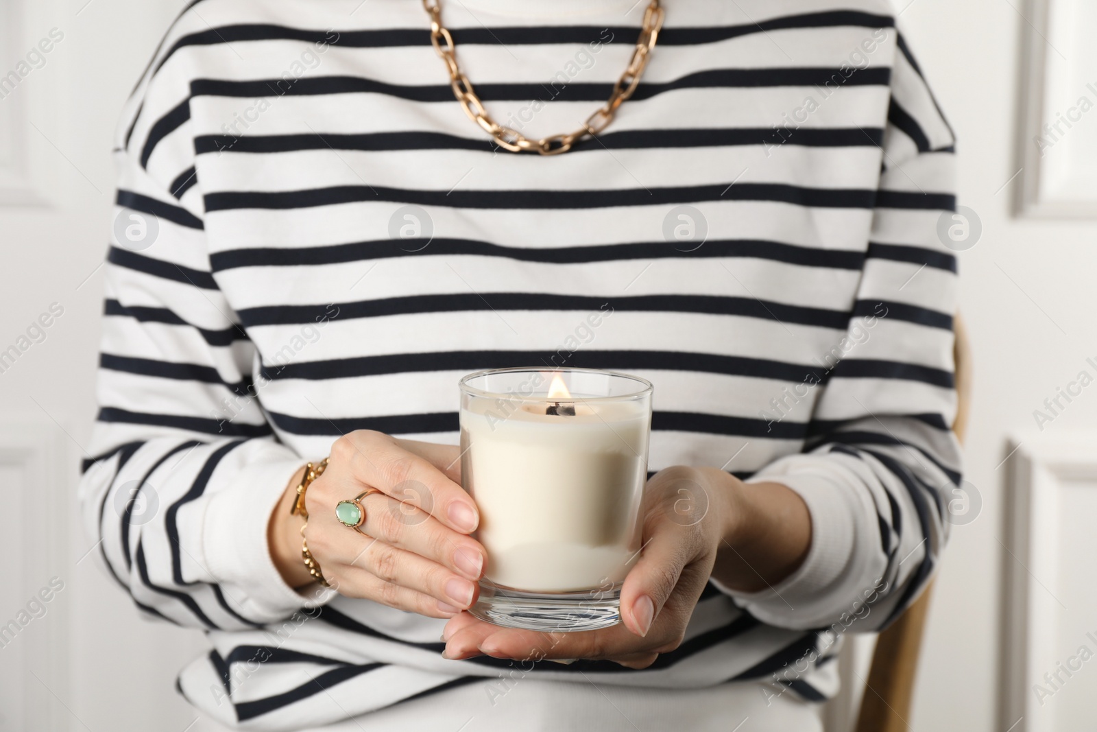 Photo of Woman with stylish jewelry holding burning soy candle on light background, closeup