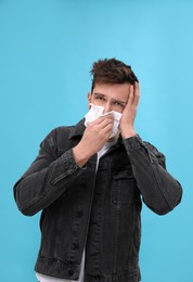 Man suffering from cold on light blue background